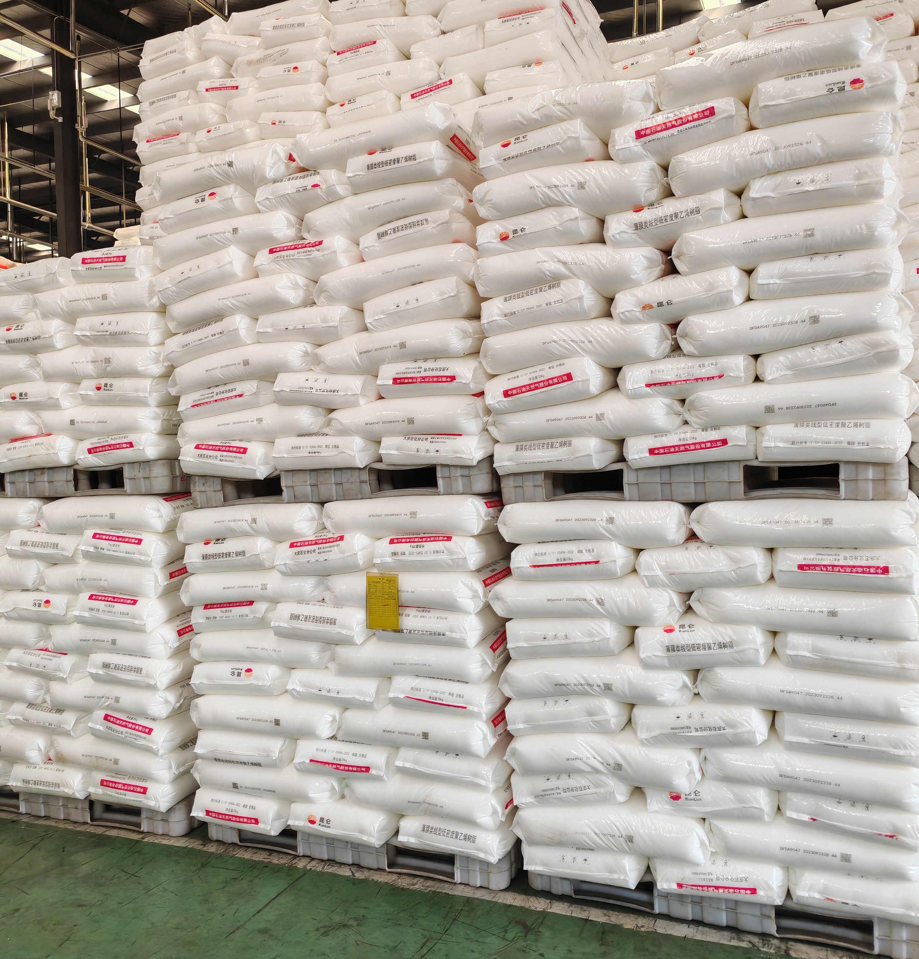 Large warehouse full stock view of Kunlun brand plastic raw material resin sacks stacked on pallets bulk storage
